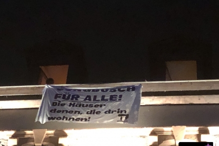 Ein Transparent hängt aus einem Fenster. Aufschrift in schwarzer Farbe auf weißem Grund: Jungbusch für alle! Die Häuser denen, die drin wohnen! In der Ecke unten rechts befindet sich das Logo der Interventionistischen Linken